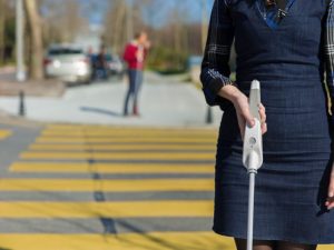 Woman in Dark dress walking across street with wewalk probing cane