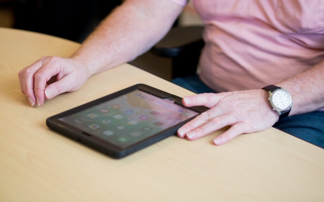 A man wearing a light pink polo shirt and a black watch on his left wrist is using his left hand to tap on an iPad